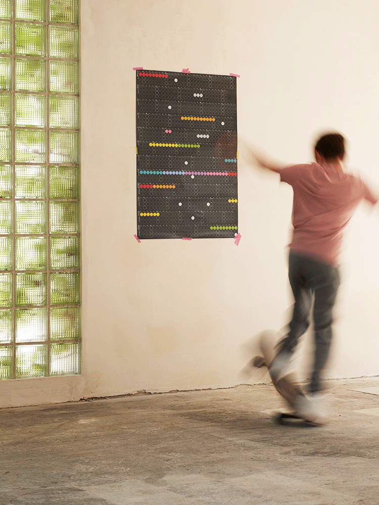 dot on Wandkalender Jahresplaner beklebt mir bunten Klebepunkten an der Wand im Vordergrund ein junger Mann auf einem Skateboard 
